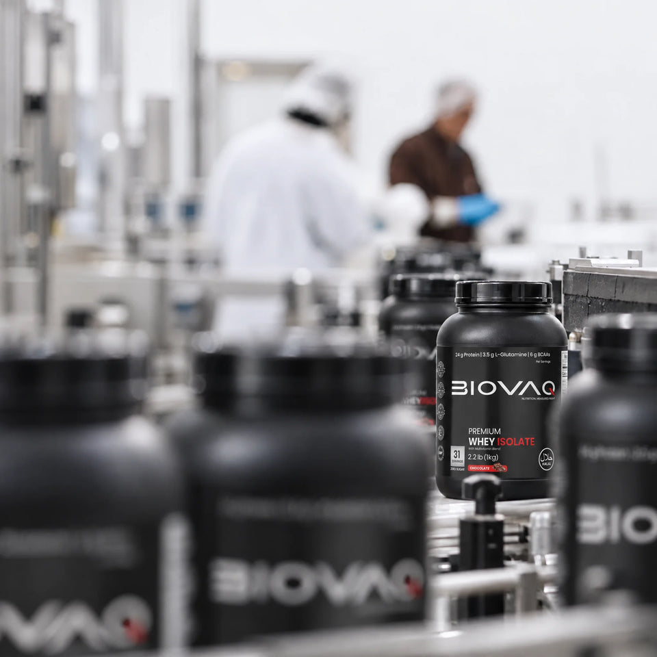 BIOVAQ Premium Whey Isolate tubs on a production line, with staff in hairnets and gloves behind